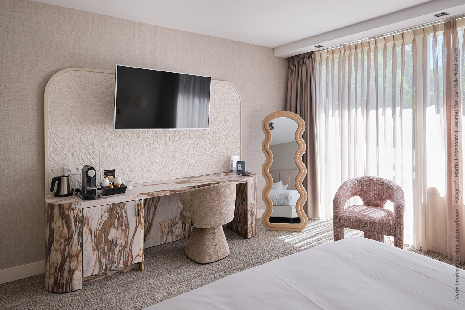 Hotelkamer met een afgerond bureau in marmerdecor D045 Fiocco, met warme bruin-witte aders en zachte tinten.