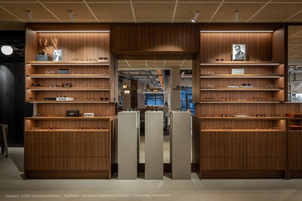 Optiekinterieur met wandmeubels in LS47 Poro Noce, een warmbruin kwartiers gezaagd walnootdecor met verticale nerf.